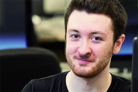 David Arivella sits in a computer lab, smiling at the camera